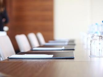 chairs lined up around a boardroom table, with water glasses and notebooks at each place